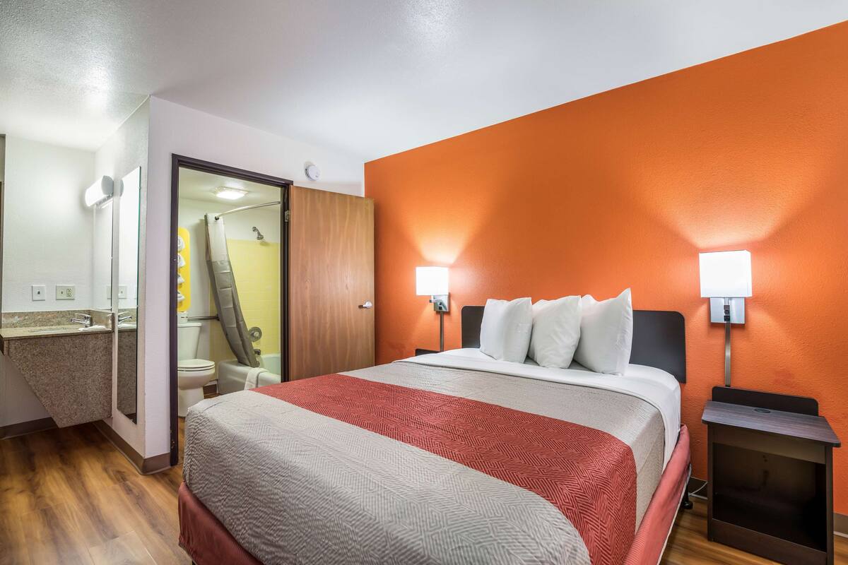 A hotel room with a bed, a nightstand, a bathroom with a shower, and a sink.
