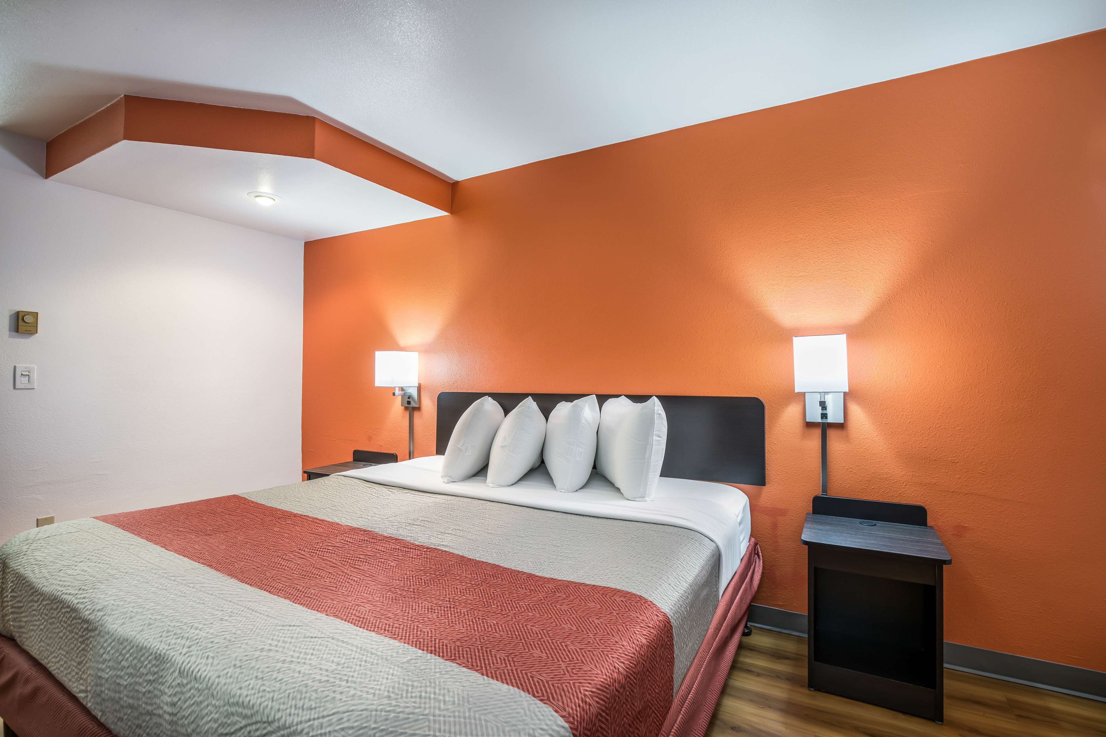 A hotel room with a large bed, two bedside tables with lamps, and a red accent wall.