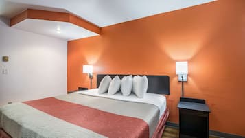 A hotel room with a large bed, two bedside tables with lamps, and a red accent wall.