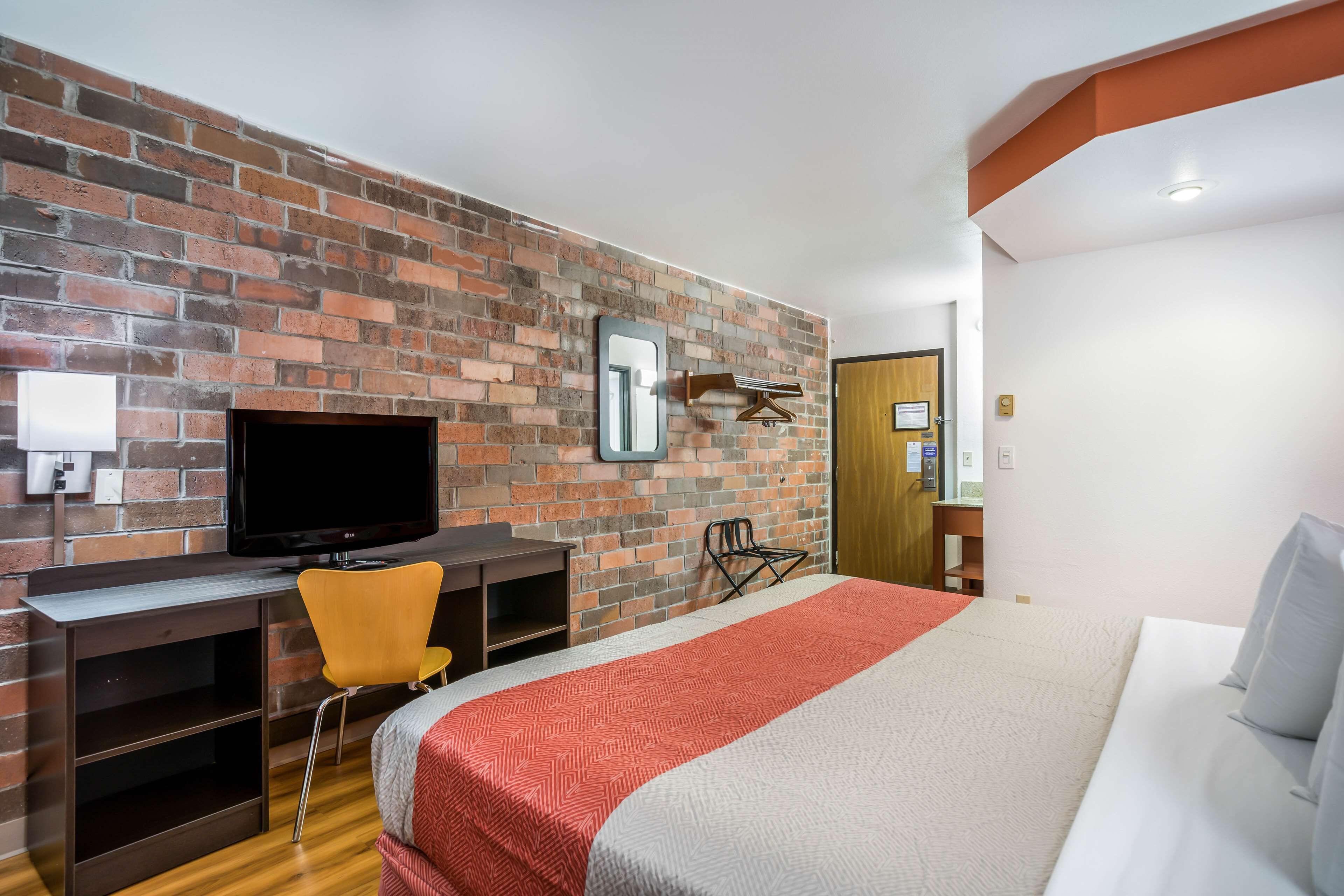 Une chambre d’hôtel avec un mur en briques, une télévision, un bureau, une chaise et un lit.