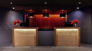 Zona de recepción con dos mostradores de madera, pared roja y tres lámparas colgantes.