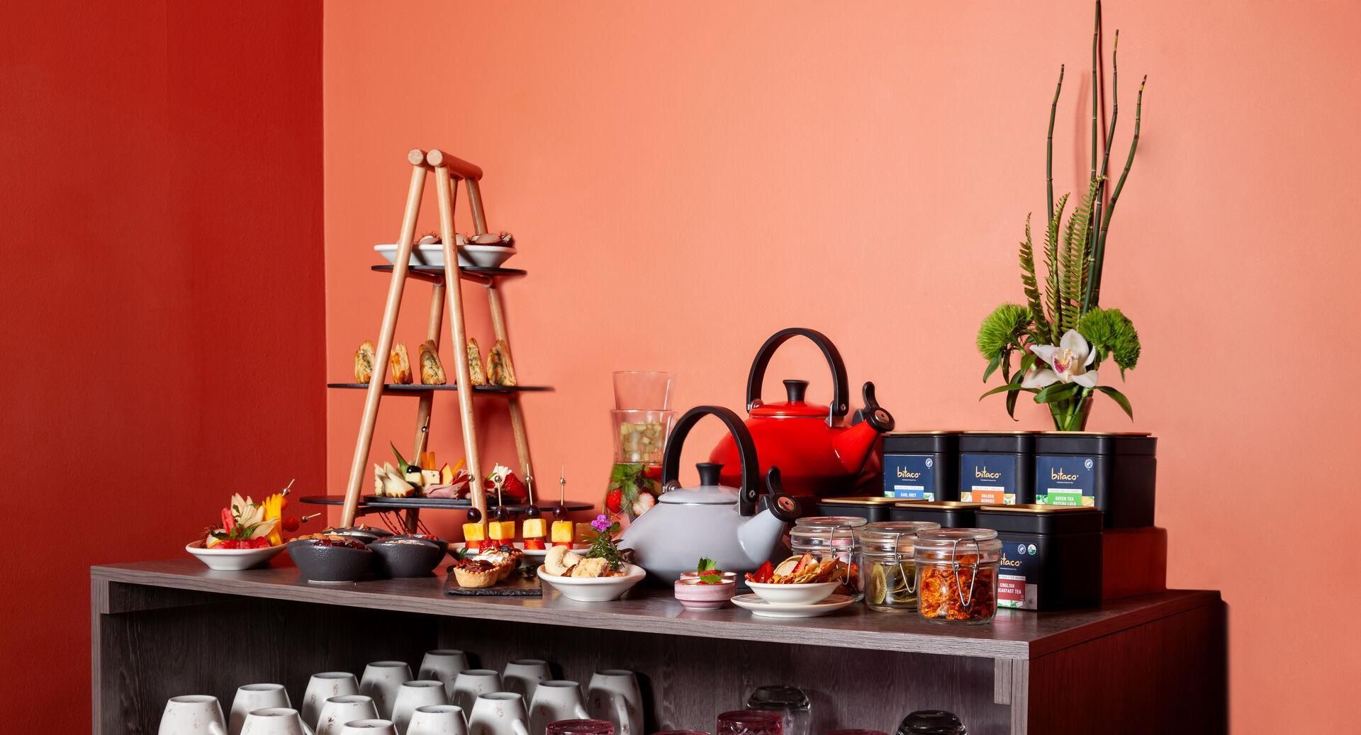 Een theeset met verschillende theecellen, een theepot en een etagère met snacks.