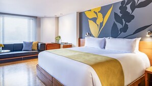 Une chambre d’hôtel avec un grand lit, un canapé, une table de chevet et un mur orné d’une fresque florale.