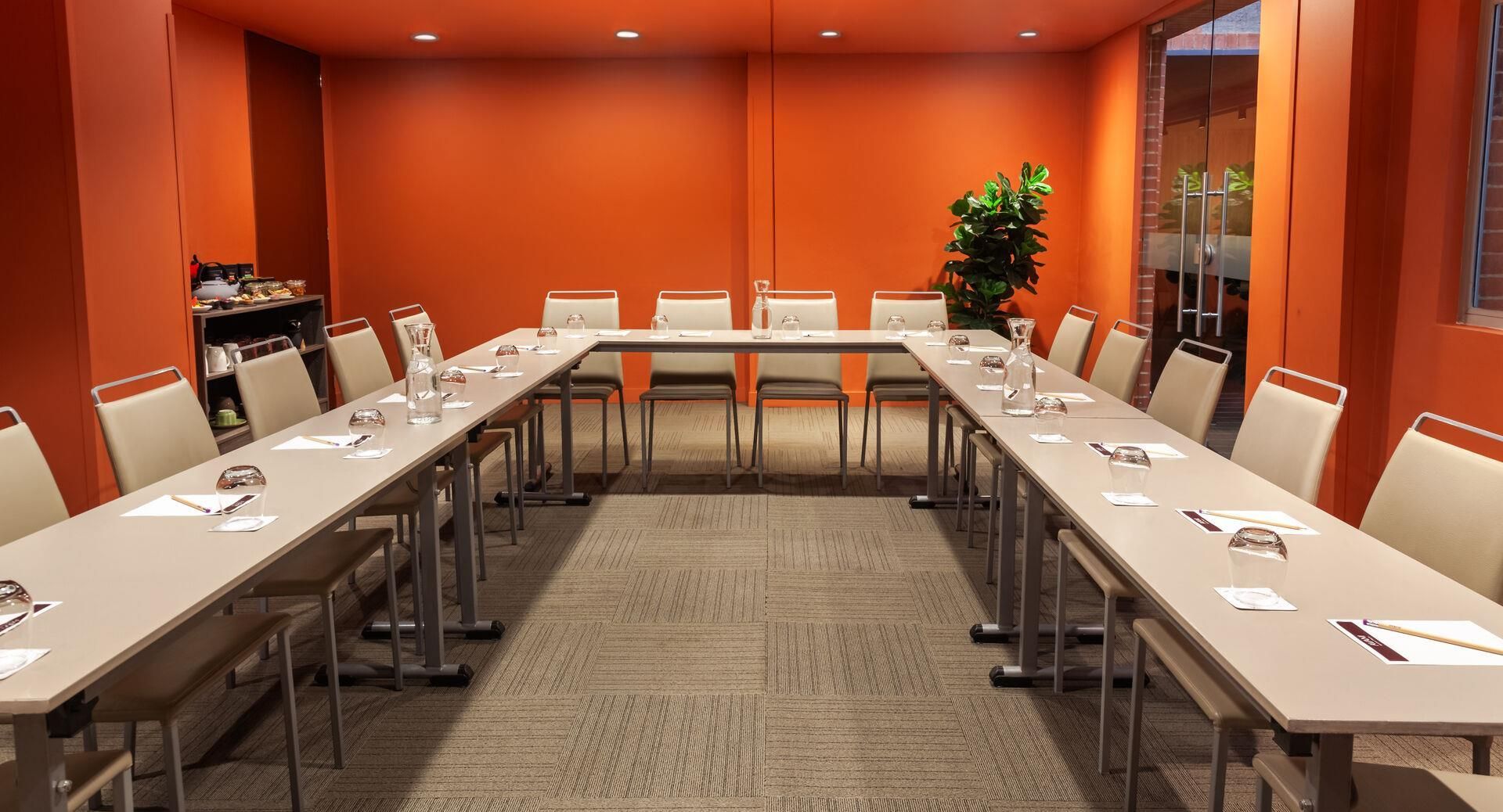 Un salón de conferencias con una mesa larga, sillas y una planta.