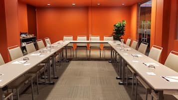 Un salón de conferencias con una mesa larga, sillas y una planta.