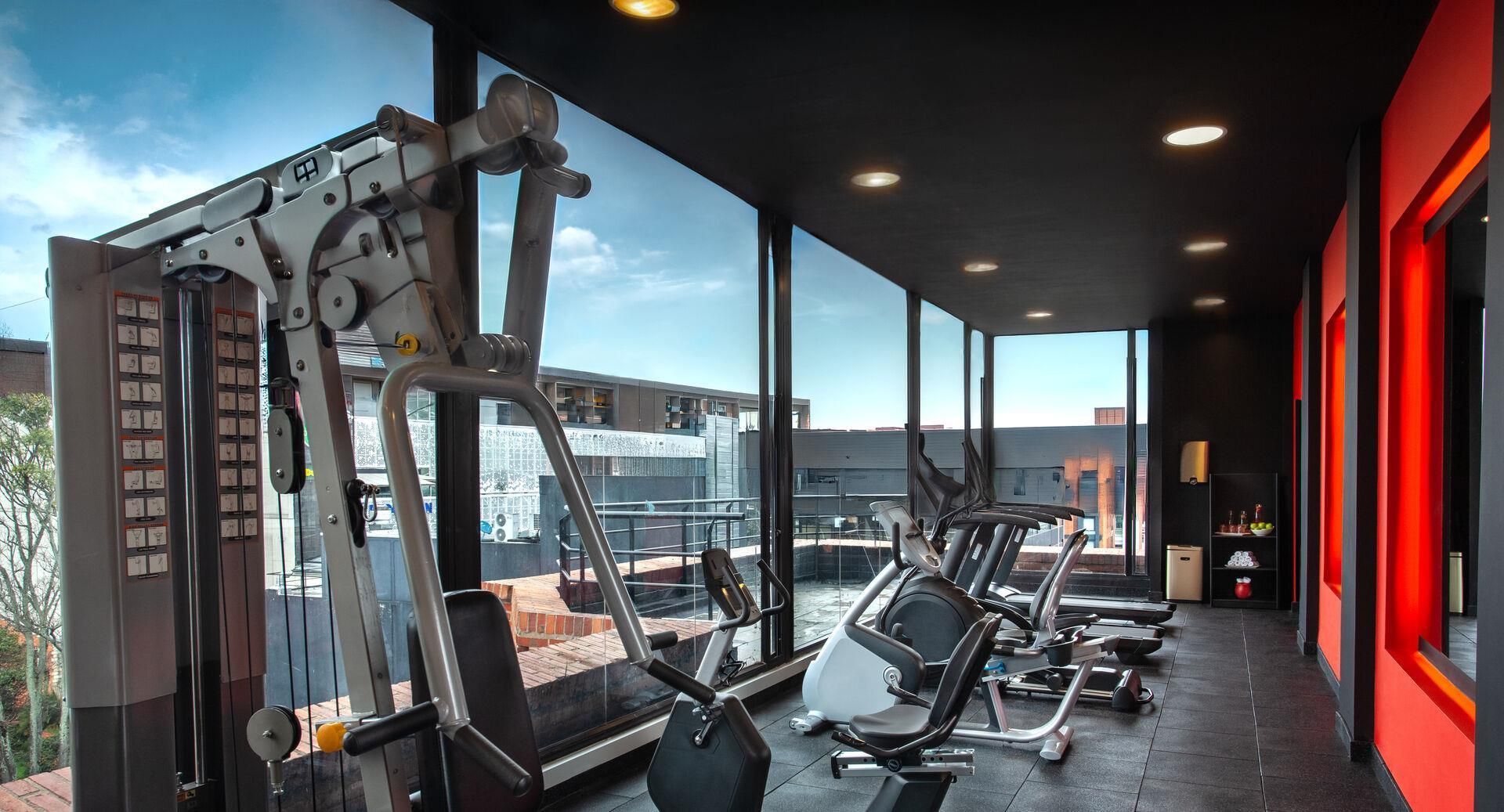 A gym with exercise equipment, large windows, and a view of buildings.