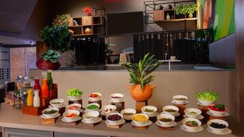 Montaje de bufé con diferentes alimentos y una planta grande en maceta.