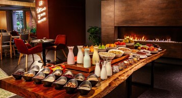 Disposición de un bufé con diferentes alimentos y bebidas, una chimenea y arreglos de asientos.
