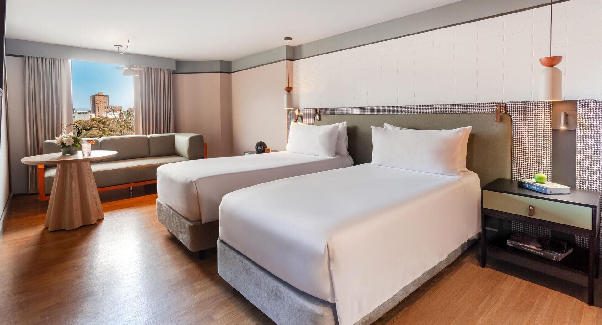 Une chambre d’hôtel avec deux lits, un canapé, une petite table et une table de chevet avec une lampe.