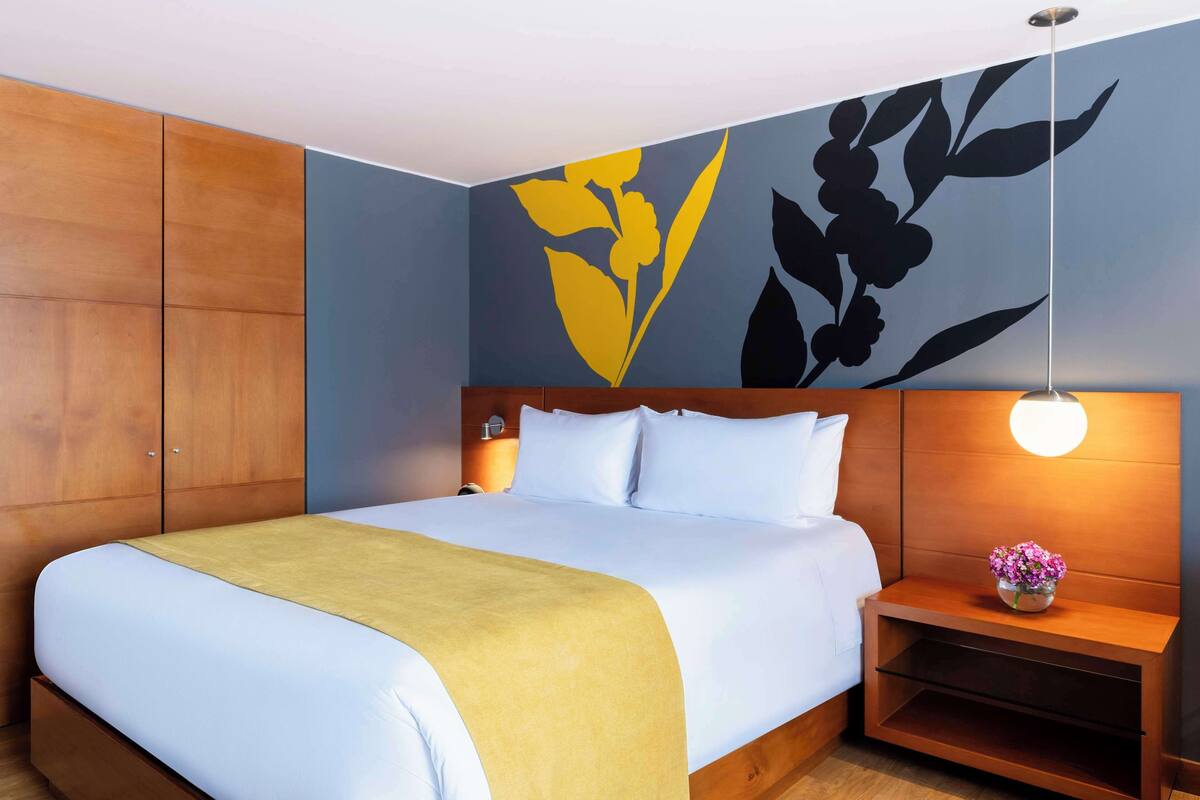 Habitación de hotel con una cama grande, un armario de madera, una mesita de noche con lámpara y una pared con diseño floral.
