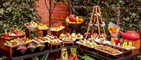 A buffet table with various food items and drinks, surrounded by greenery.