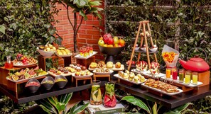 A buffet table with various food items and drinks, surrounded by greenery.