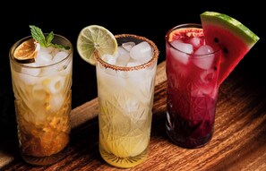 Drie glazen met ijskoude drankjes en garnering op een houten ondergrond.