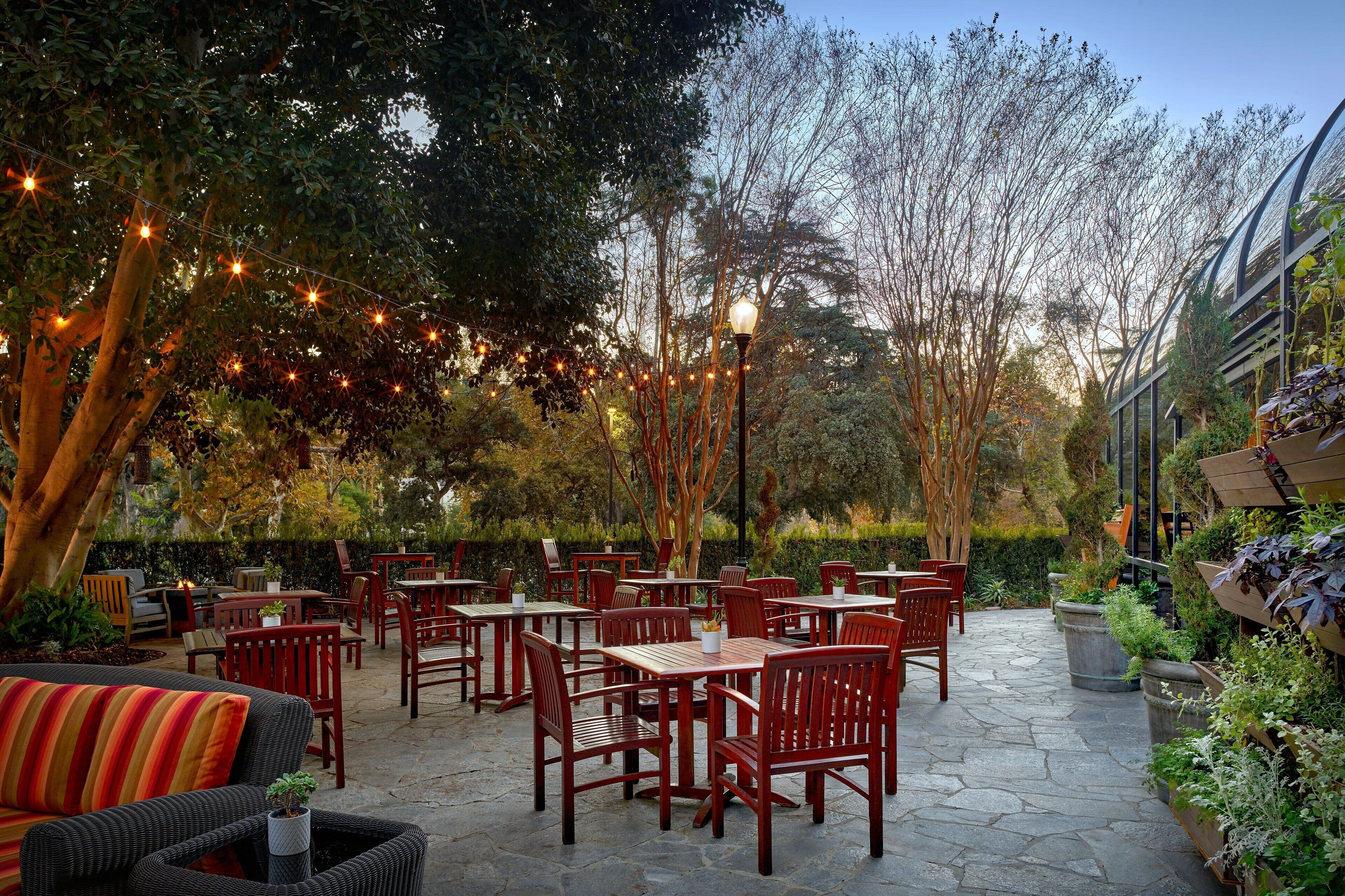 An outdoor patio area with wooden tables and chairs, string lights, and potted plants.