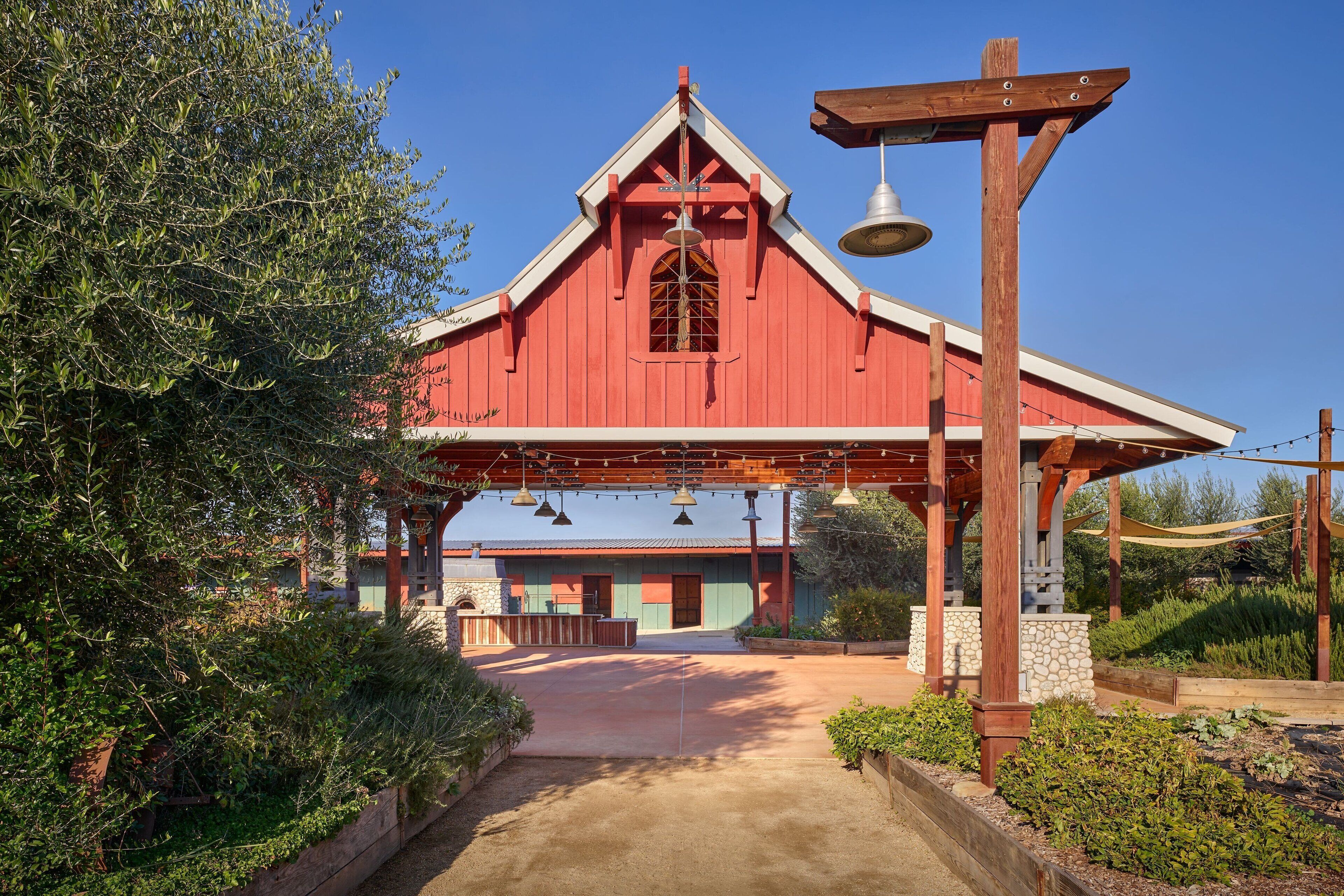 A red barn-style building with a bell tower, surrounded by greenery and a paved pathway.