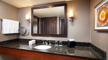 A hotel bathroom with a granite countertop, a round mirror, a white sink, and two wall-mounted lights.
