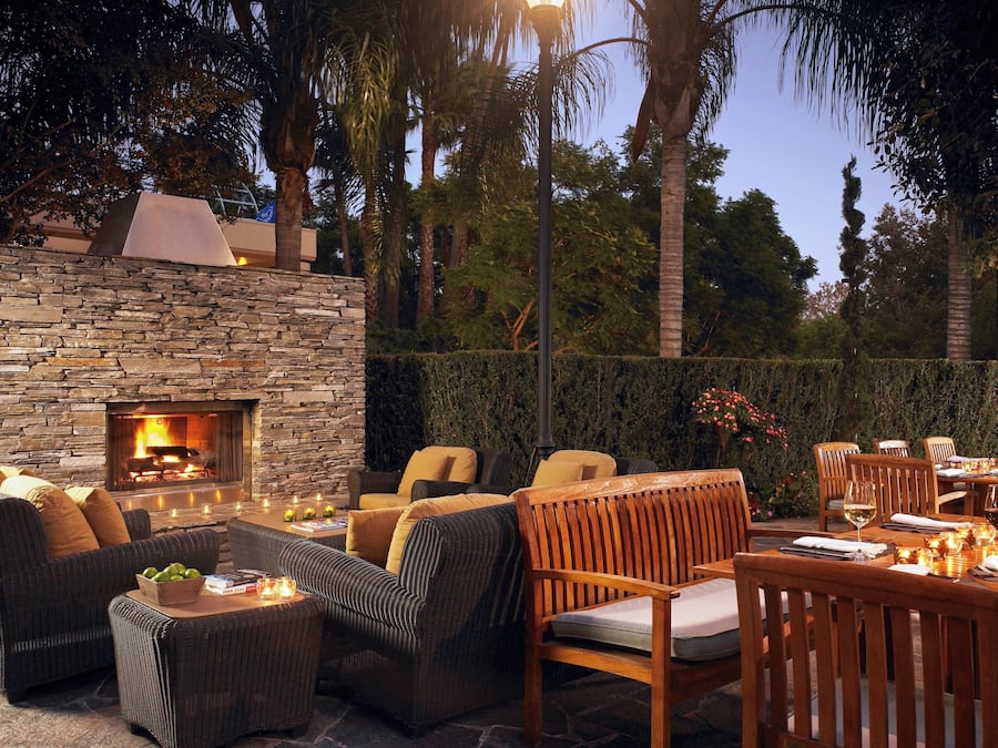 Un patio al aire libre con muros de piedra, una chimenea de piedra, mobiliario de mimbre y una mesa de comedor lista para una comida.