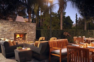 An outdoor patio with stone walls, a stone fireplace, wicker furniture, and a dining table set for a meal.