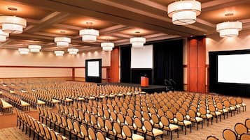 Un salón de conferencias con filas de sillas, un escenario y una pantalla grande.