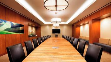 A conference room with a long table, black chairs, a large painting, a flat-screen TV, and a ceiling light fixture.