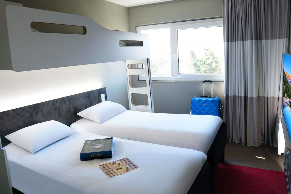 Une chambre d’hôtel avec un lit, une valise, une fenêtre avec des rideaux et un téléviseur.