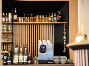 Uma área de bar com diversas garrafas de bebidas, copos de vinho e uma máquina de café.