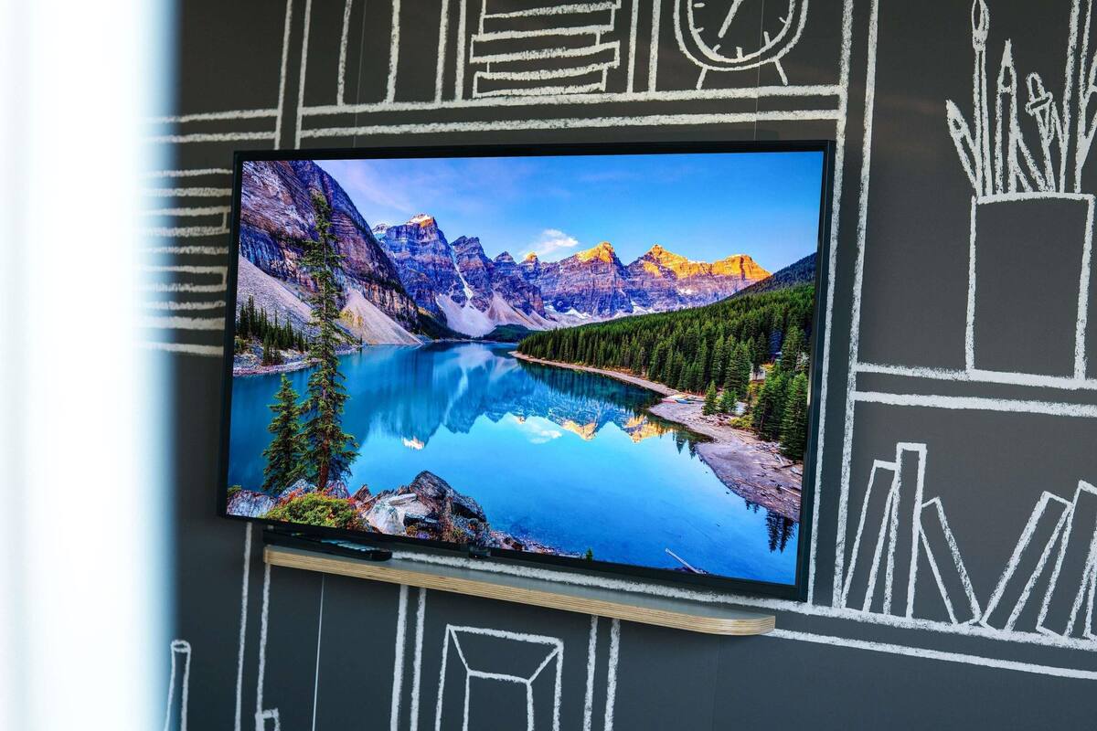 Un téléviseur fixé au mur, reflétant un paysage de montagne sur une étendue d’eau.