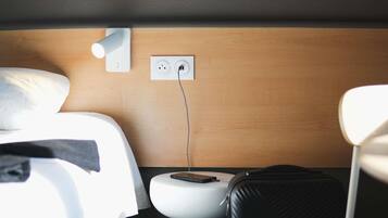 A hotel room with a bed, a bedside table with a phone, a power outlet, and a suitcase.