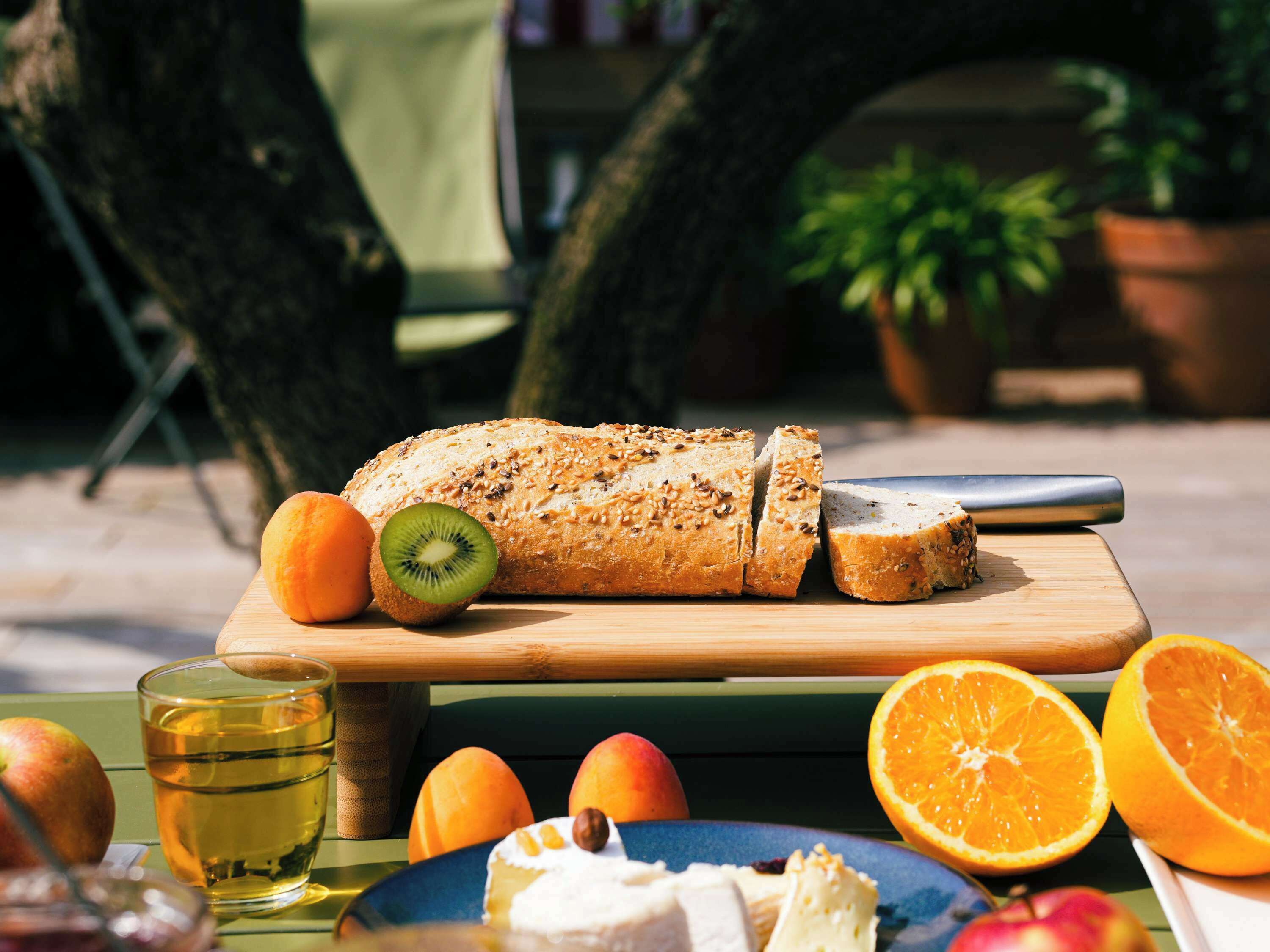 A picnic setup with bread, fruits, and a beverage on a table.