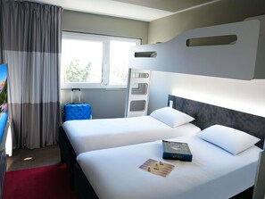 Ein Hotelzimmer mit zwei Betten, einem Fenster, einem roten Teppich und einem Koffer.