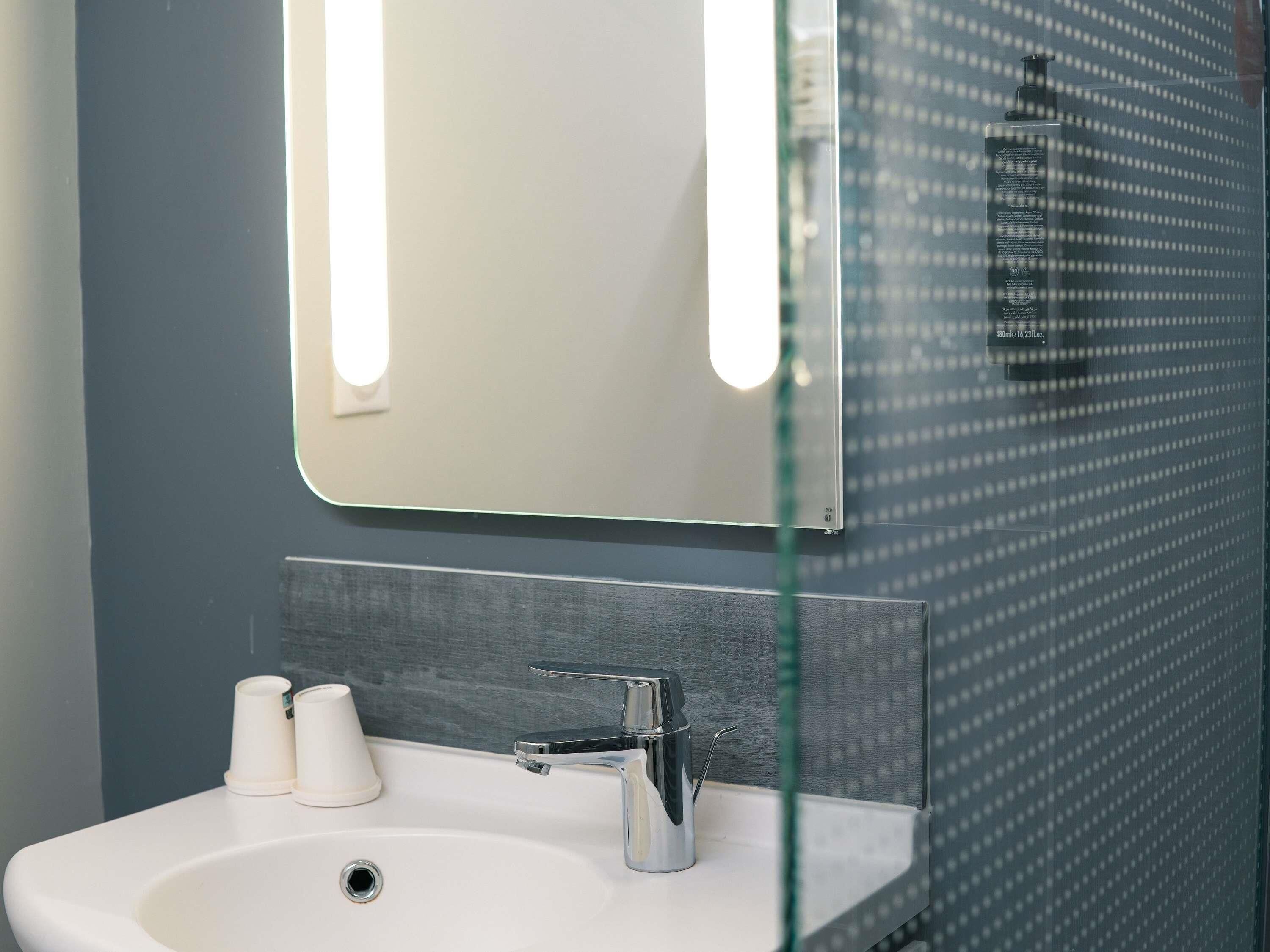 Un baño con lavamanos blanco, grifo cromado y cabina de ducha con paredes de vidrio.