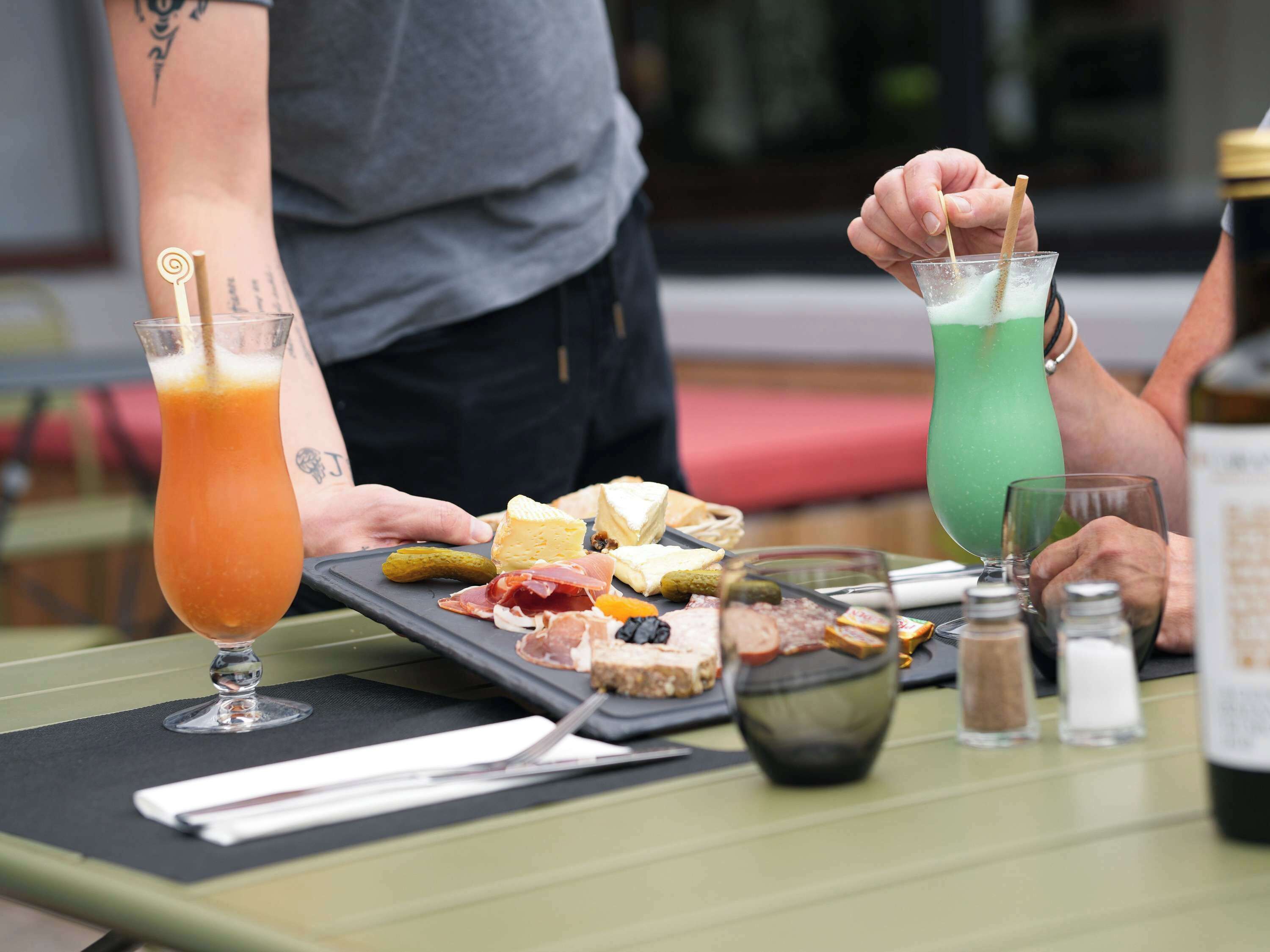 Une table garnie d’une variété d’aliments et de boissons, notamment une boisson verte, du fromage, de la charcuterie et des cornichons.