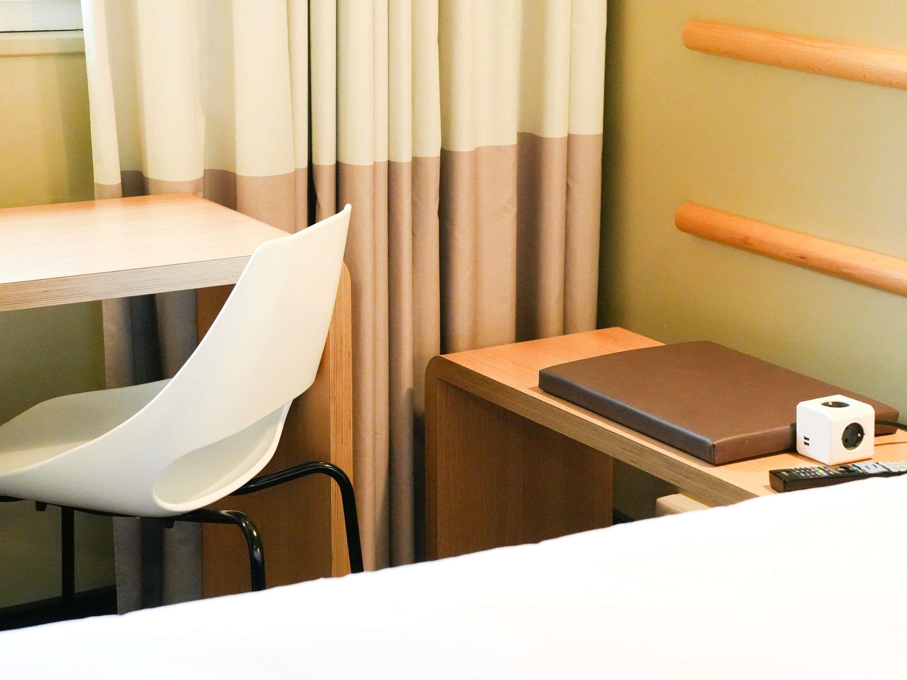 Habitación de hotel con cama, escritorio, silla, control remoto y un altavoz pequeño.