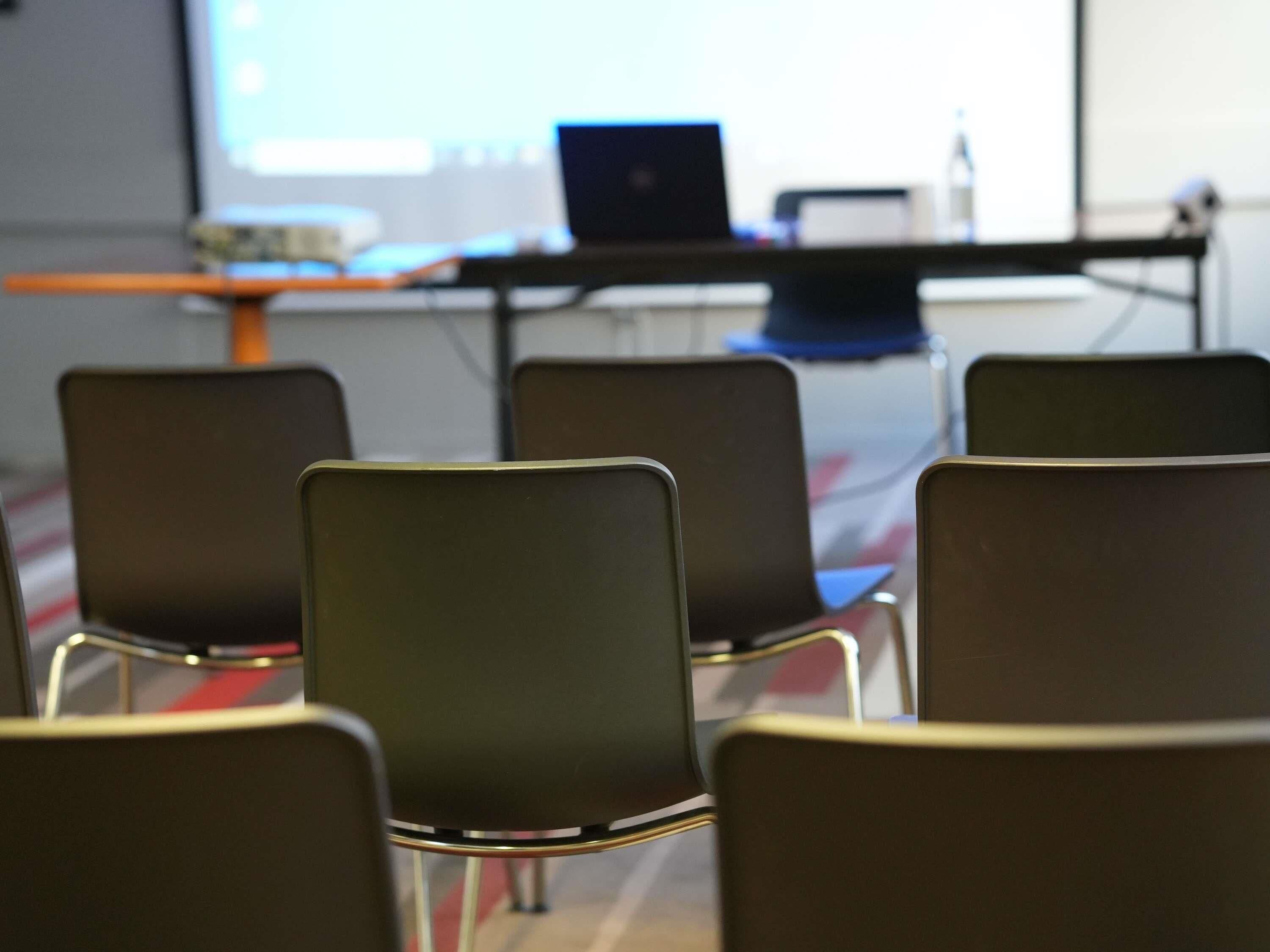 A conference room with a laptop on a table, several chairs, and a projector screen in the background.