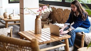 A person using a laptop on a wooden table with a vase of flowers. - ibis Caen Porte d'Angleterre (Herouville-Saint-Clair)