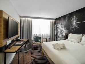A hotel room with a bed, a desk with a computer, a chair, a TV, and a window with curtains. - Novotel Wroclaw City (Wroclaw)
