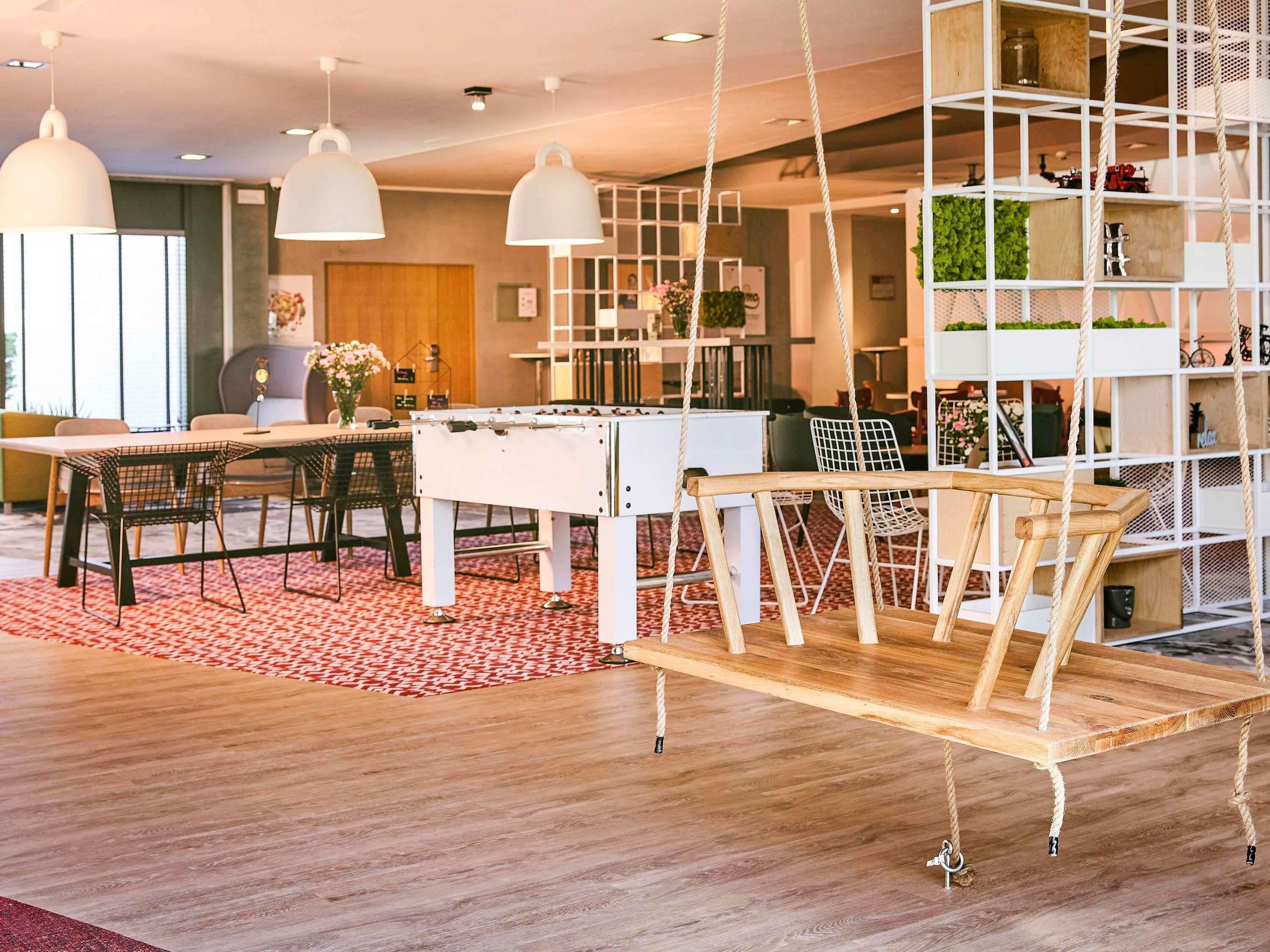 Un salon moderne avec un baby-foot, des fauteuils suspendus et une balançoire en bois.