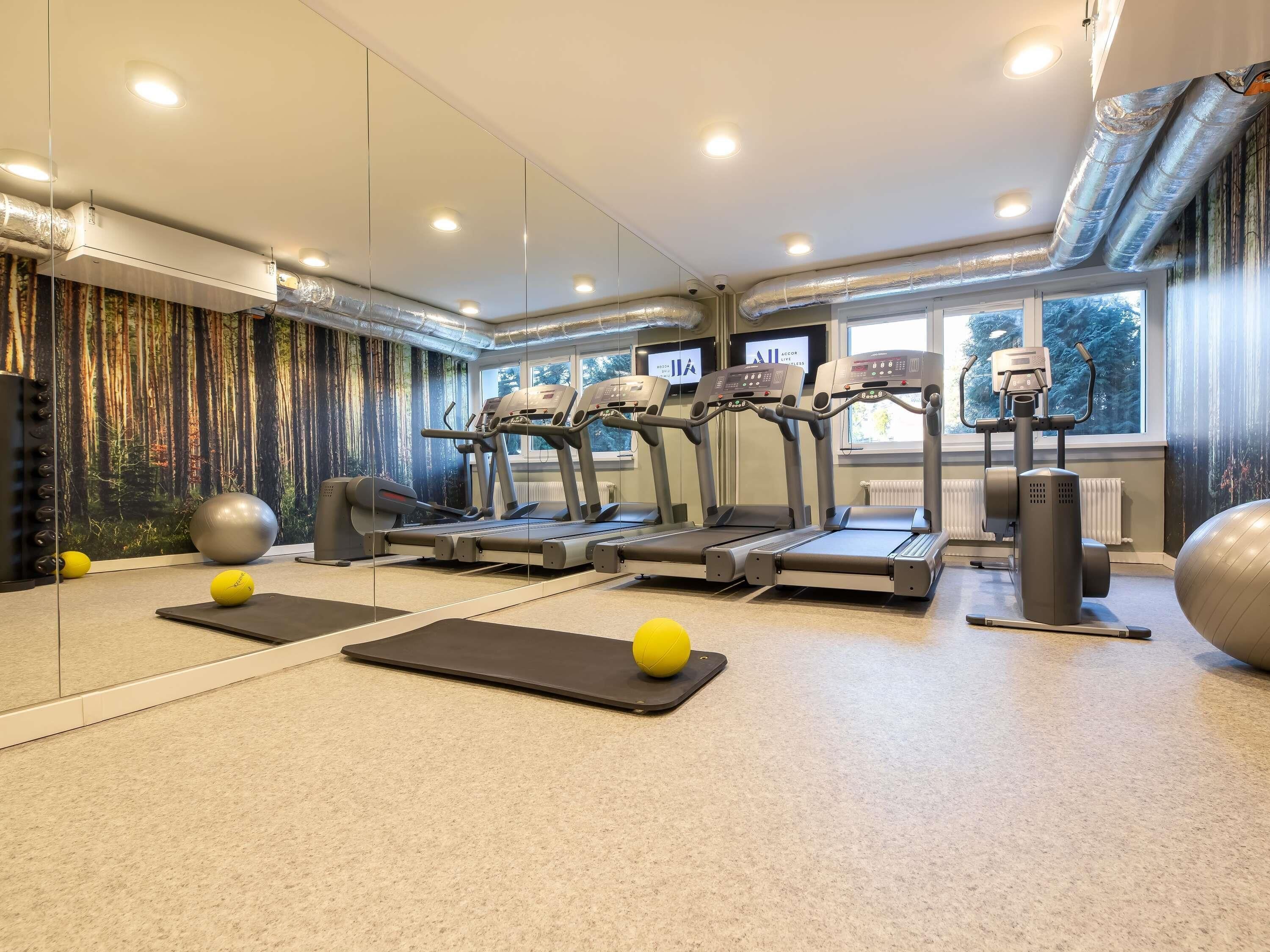 Une salle de sport équipée de tapis de course, de ballons d’exercice et d’un mur recouvert de miroirs.