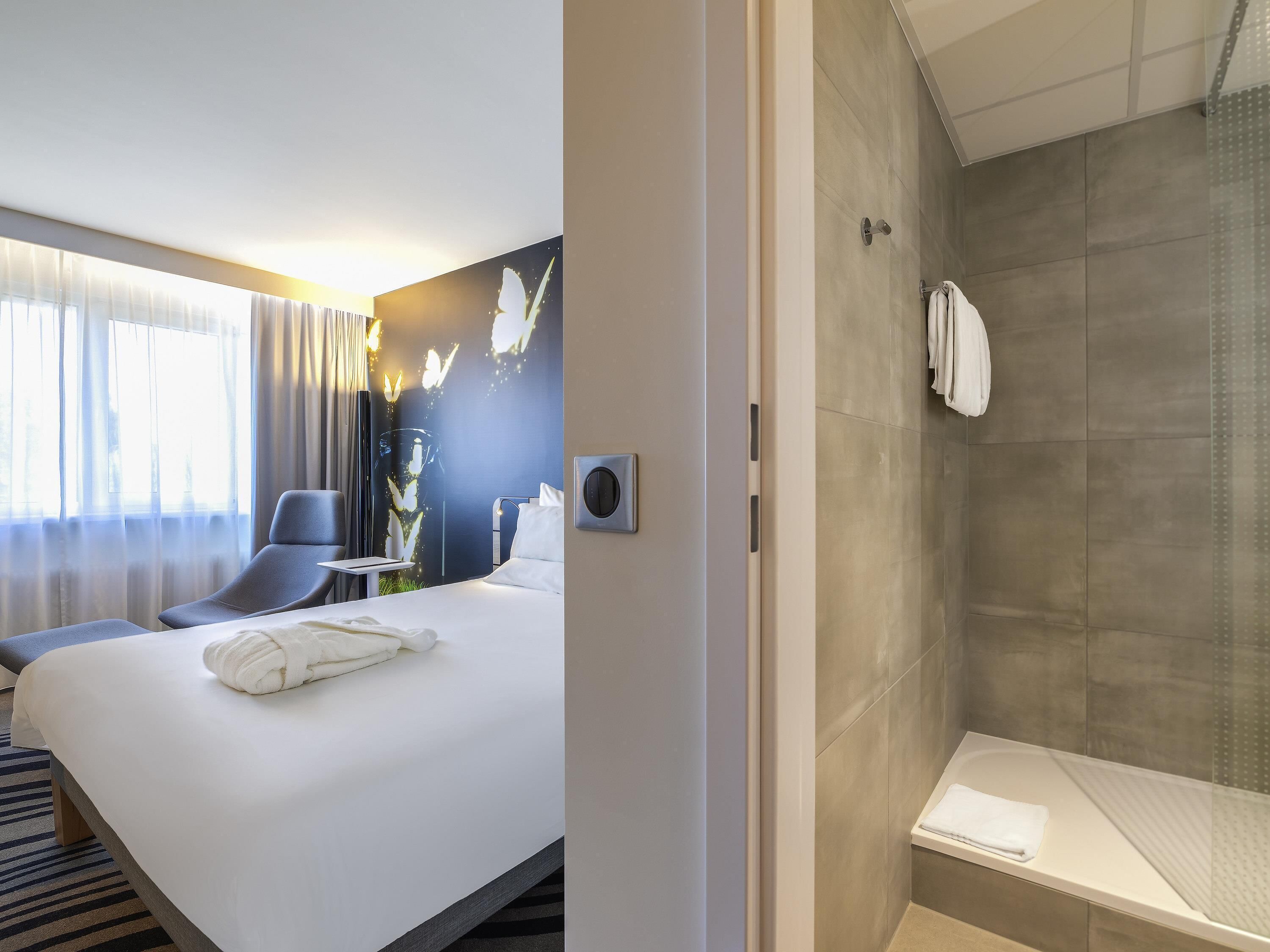 A hotel room with a bed, a chair, a desk, a shower area, and a wall with a butterfly mural.