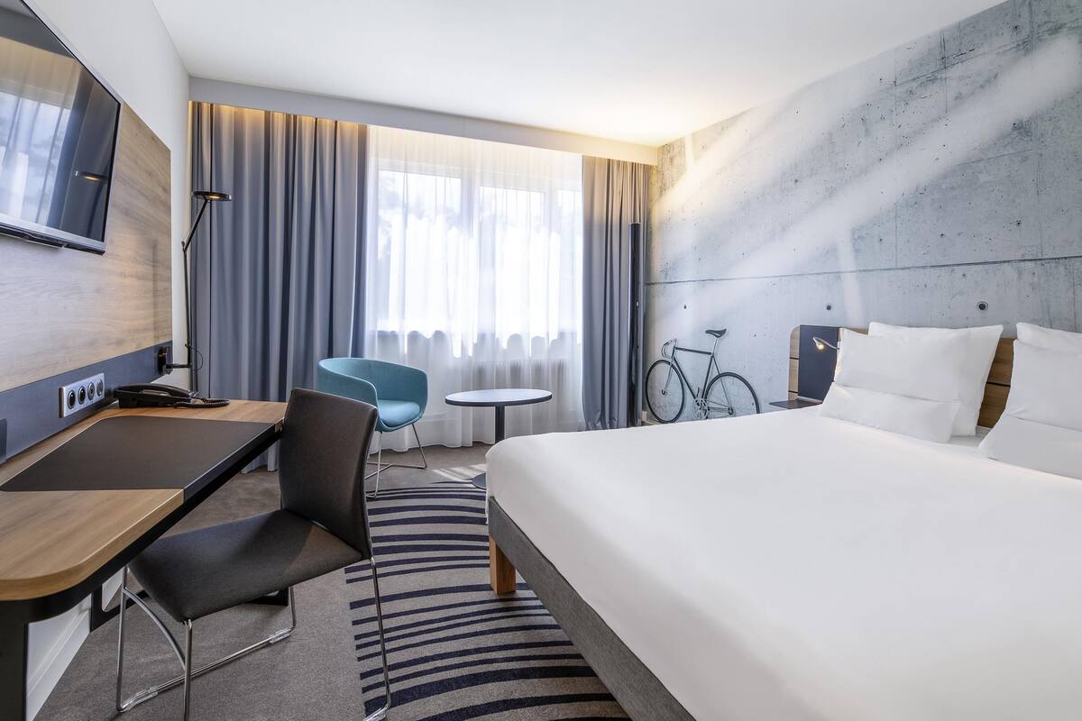 A modern hotel room with a bed, desk, chair, and bicycle.