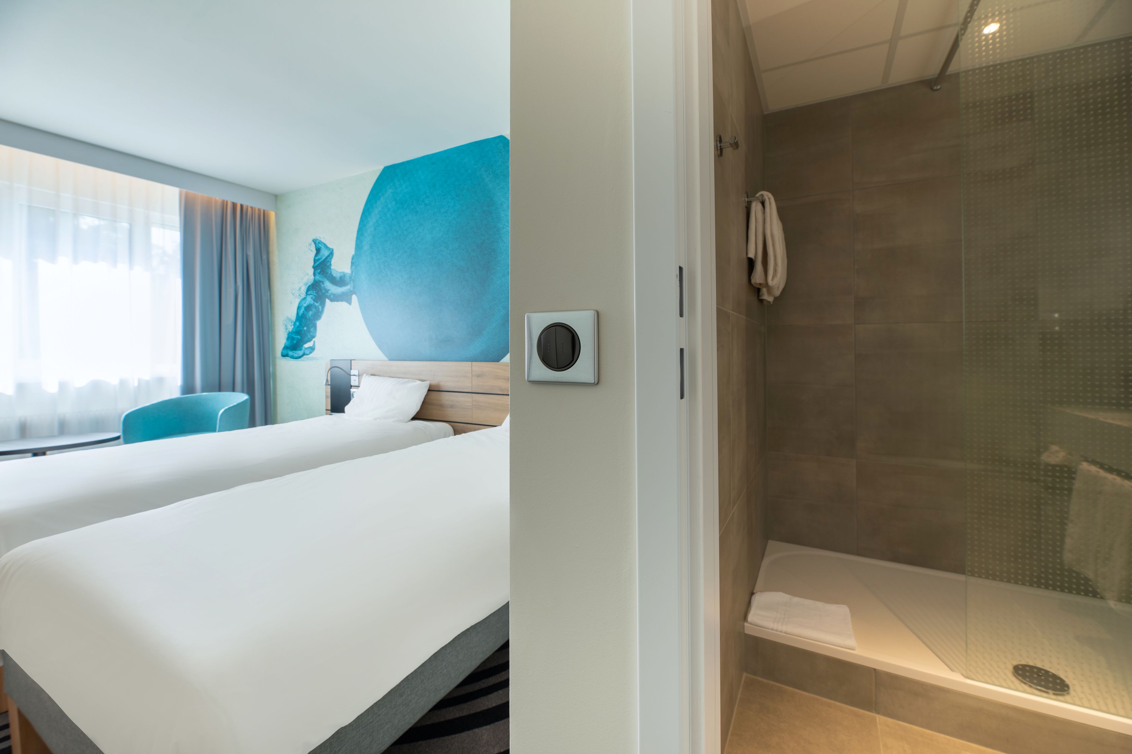 Een hotelkamer met twee bedden, een douche en een groot raam met gordijnen.