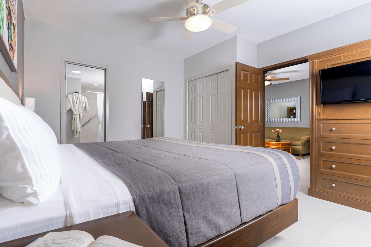 Een slaapkamer met een bed, een plafondventilator, een televisie en een houten dressoir.