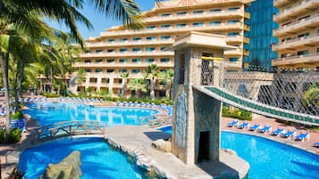A hotel with a large swimming pool, palm trees, and a bridge.