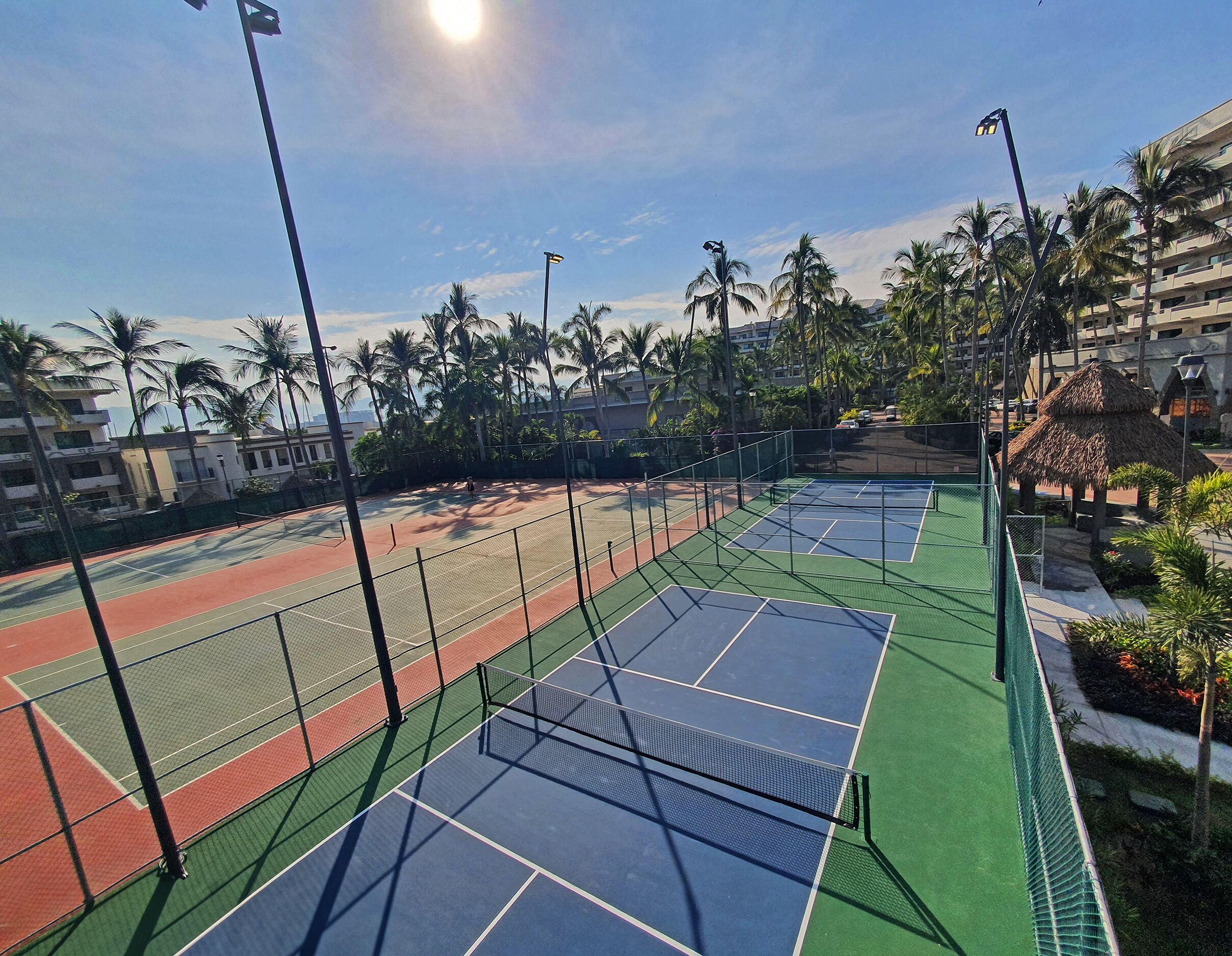 A tennis court with multiple courts, surrounded by palm trees and buildings.