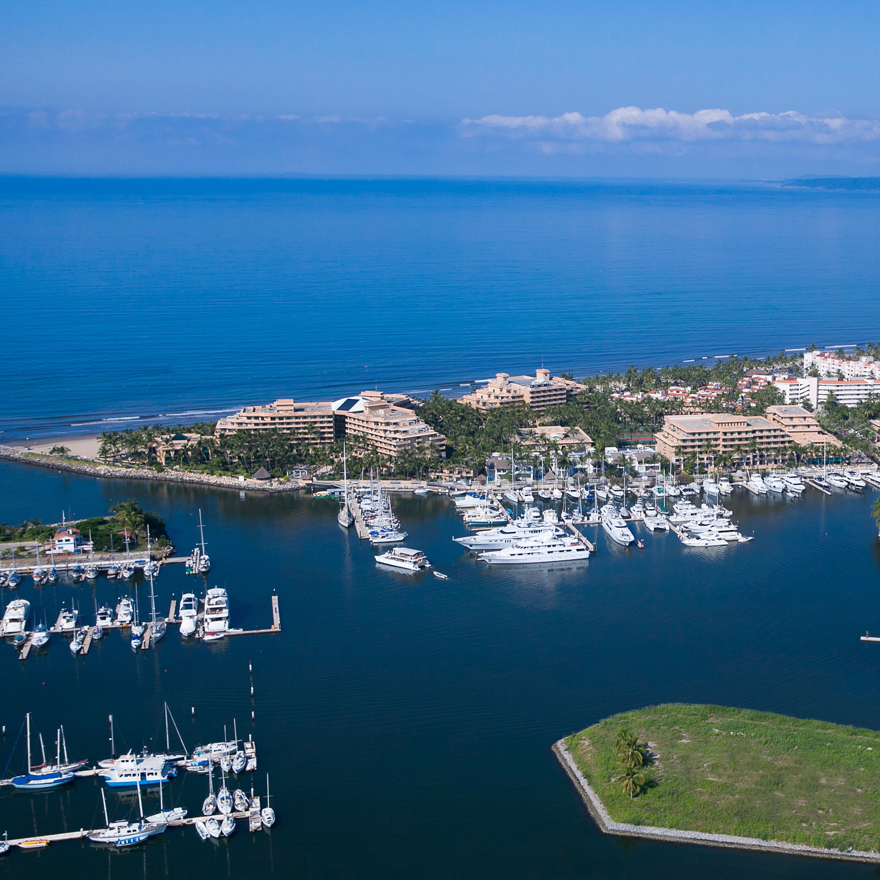 An aerial view of a marina with numerous boats docked, surrounded by buildings and palm trees.