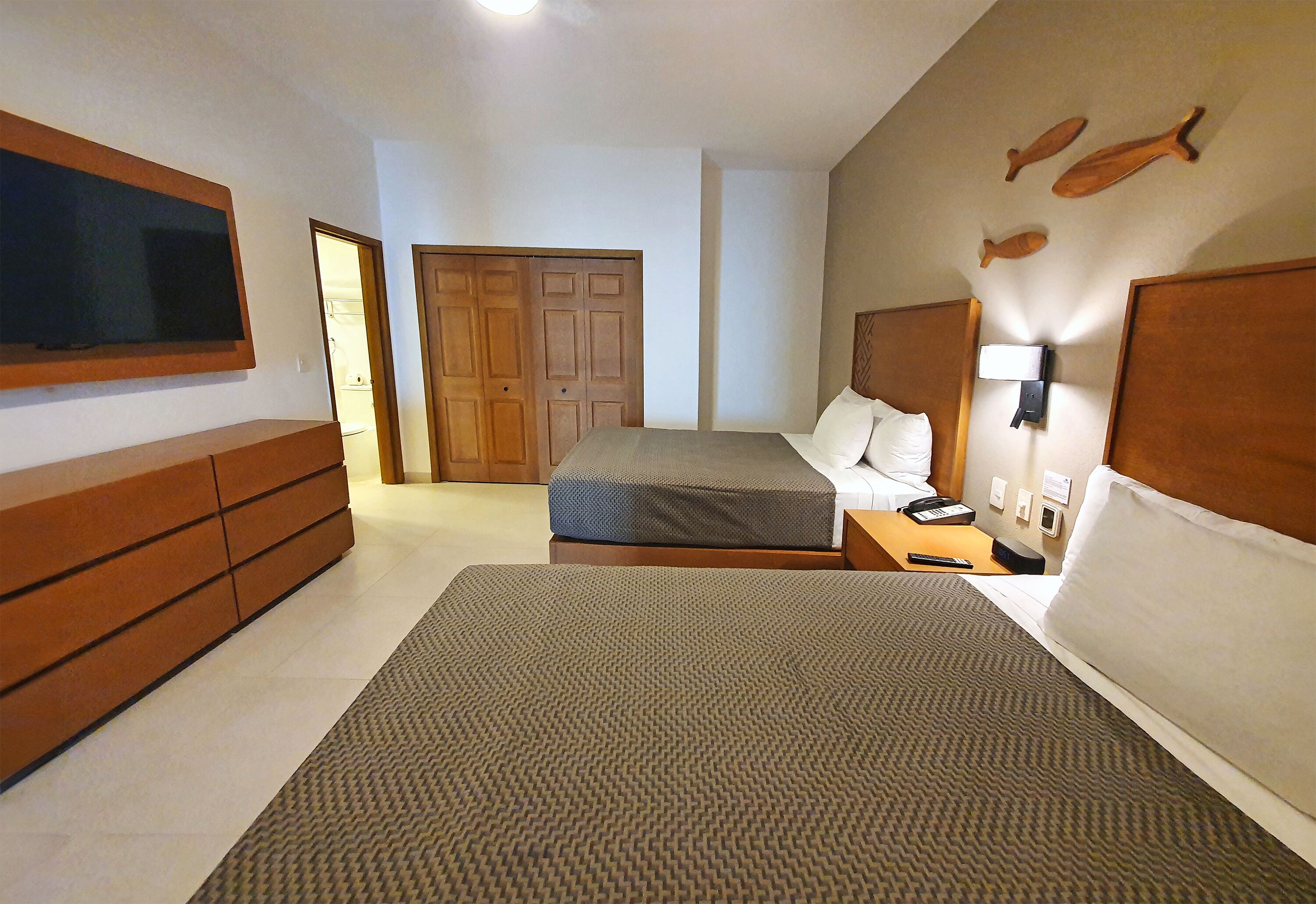 A hotel room with a large bed, a bedside table with a lamp, a wardrobe, and a television on the wall.