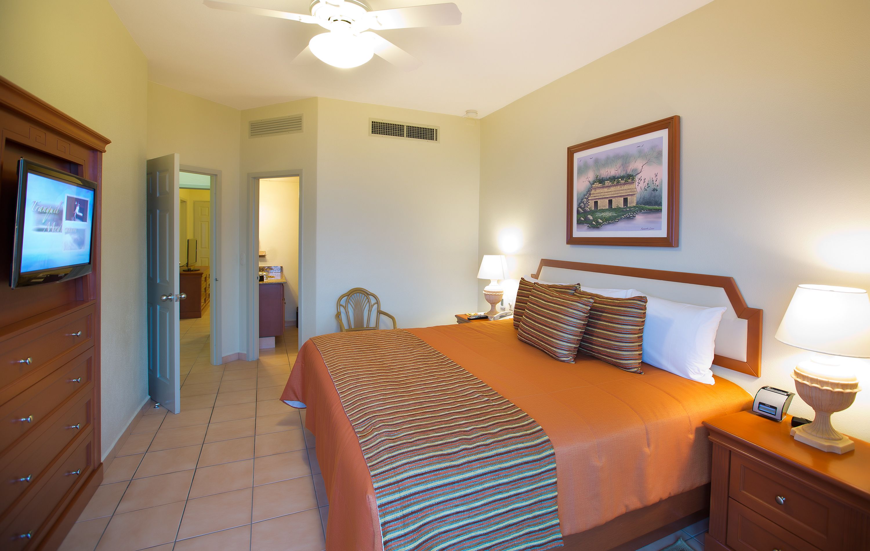 A hotel room with a bed, a television, a nightstand, a lamp, and a painting on the wall.