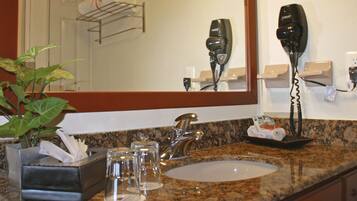 A bathroom with a granite countertop, a sink, a mirror, a hairdryer, and a towel rack with towels.