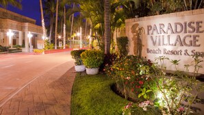 Señal para Paradise Village Beach Resort & Spa, rodeada de palmeras y jardines bien cuidados.