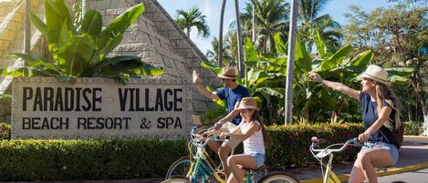 Schild für Paradise Village Beach Resort & Spa mit einer Steinstruktur und Palmen im Hintergrund.